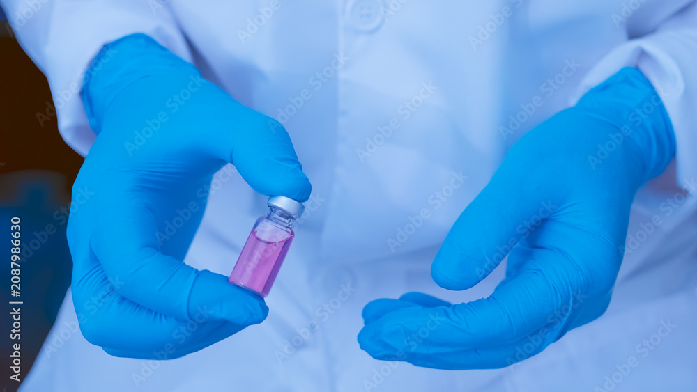 Fototapeta premium Scientist wearing gloves holding a medical vial with pink liquid solution