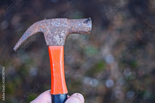 hand holding one brown iron rusty hammer with red handle on day street