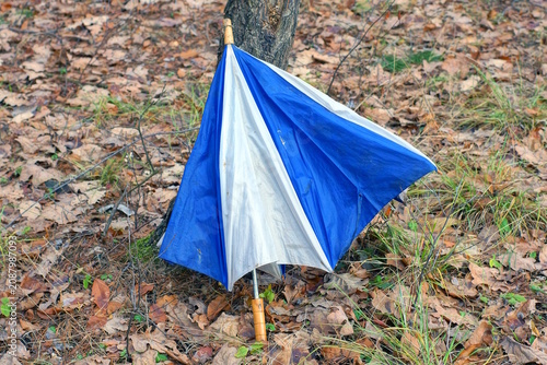 one blue white dirty broken umbrella with brown wooden handle lies on ground in the street