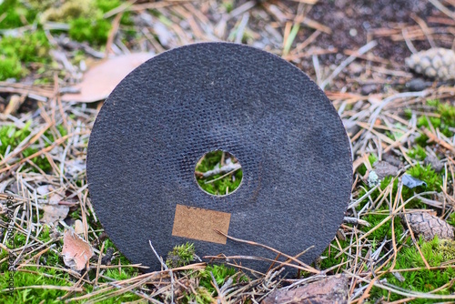 one black cutting wheel for an angle grinder lies on green moss on the street