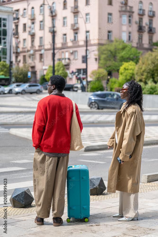 Naklejka premium African american man and woman travelers visiting new country on holiday together, married couple with luggage standing on street looking around downtown, black male and female tourists on vacation.
