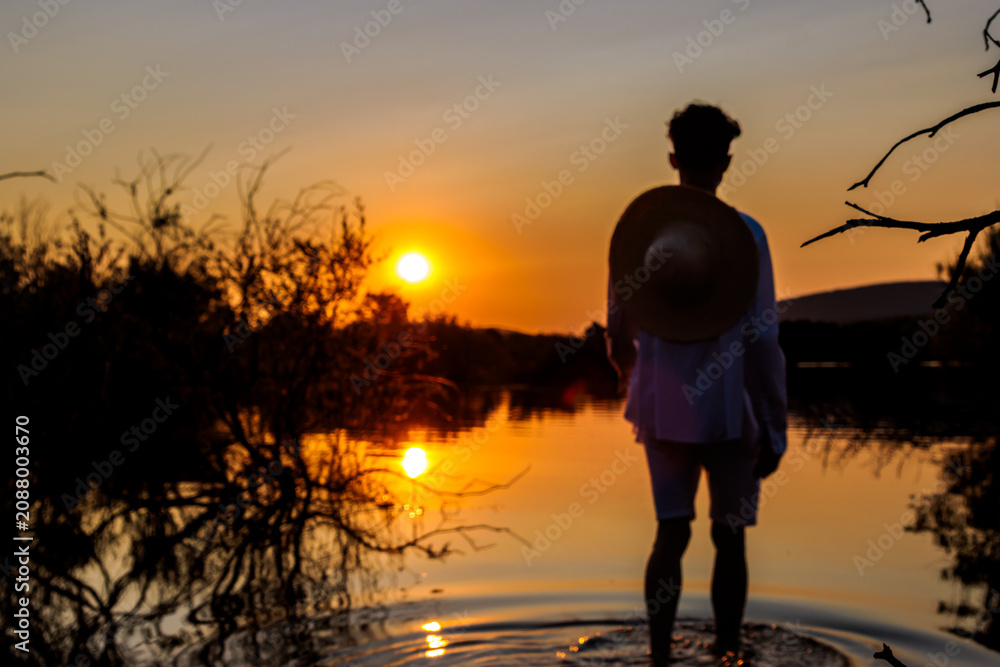 Fototapeta premium Person standing in water watching summer sunset over lake with reflections