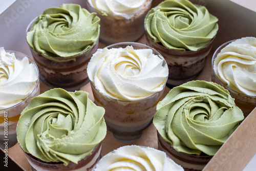 Tableau sur toile Chocolate trifle desserts in clear plastic cups with green and white cheese cream topping, top view on a horizontal culinary background