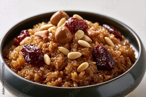 Korean sweet rice yakbap with jujubes, chestnuts and pine nuts in dark bowl, traditional holiday food close up
