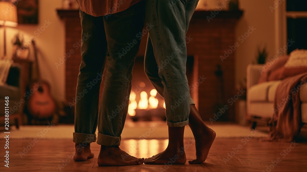 Obraz premium Interracial couple slow dancing barefoot in warm living room