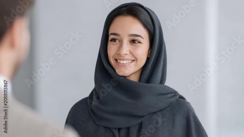Young smiling woman wearing dark headscarf looking at person in office environment with casual interaction and positive expression