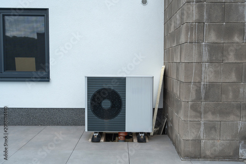 installed stationary air conditioning unit on residential building exterior side view neutral functional gray white concrete block wall setting natural light clean background.
