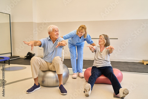 Seniors practicing rehabilitation exercises with assistance on stability balls in rehab facility