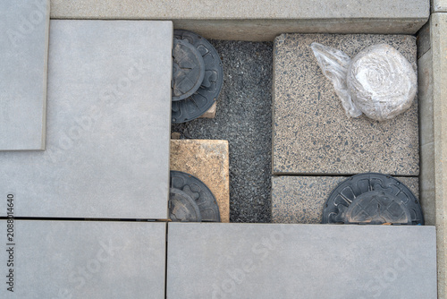 pavement tiles on outdoor concrete area with black circular objects and plastic bag in top-down perspective. neutral mood, urban environment, construction setting.