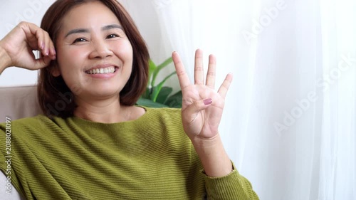 Happy Asian woman age 40 smiling and showing four fingers hand sign at home. Cheerful beautiful mature middle-aged female looking at camera, Midlife Confidence, Well-being concept