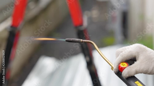 Close-up of a worker holding a gas blowtorch with an open orange flame outdoor. Industrial roofing or construction process, plumbing heating torch tool concept