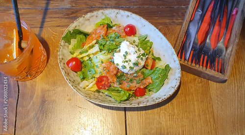 Appetizing salad with salmon, cherry tomatoes, herbs and stracciatella cheese on a wooden table next to a refreshing