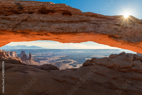 Majestic sunrise illuminates Mesa Arch in Canyonlands National Park, Utah, painting iconic landscape with warm sunlight. Morning light creates breathtaking natural view at dawn