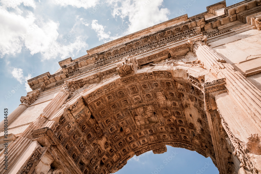 Obraz premium Low angle view of a carved ancient Roman triumphal arch with coffered ceiling, columns and ornamental reliefs