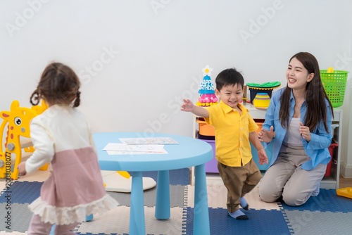 Children play in a colorful room while a teacher watches and encourages them during an activity