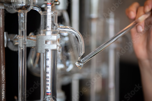 Canvas Print Macro shot of a clear liquid droplet falling from a glass distillation tube next to a hydrometer in a laboratory