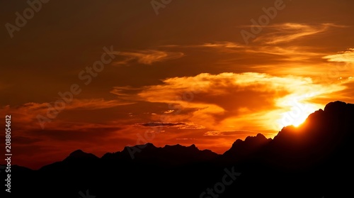 Dramatic sunset over silhouetted mountain peaks with vibrant orange and red sky, serene and peaceful atmosphere