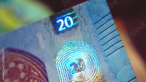 A close-up of the security strip with holographic emblems on the 20-euro banknote. Glowing security holograms on the 20-euro banknote. 4K macro slow motion video at 60 fps.