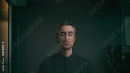 Young adult man with dark hair in black collared shirt, neutral expression, direct eye contact, indoor professional portrait against dark minimalist background