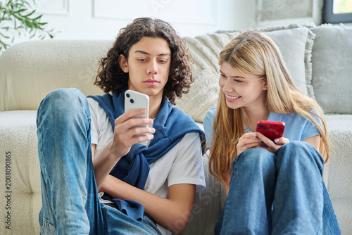 Teenage boy showing something on smartphone screen to smiling girl