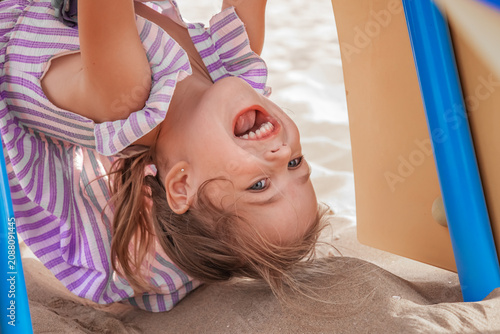 Obraz na płótnie Laughing little girl upside down under playground on sandy beach