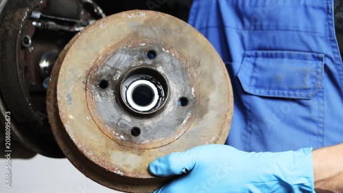 A man in blue overalls and gloves holds a car's brake drum, car repair and maintenance.
