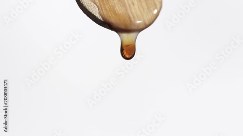Brown cosmetic product dripping from spatula, macro, neutral background.