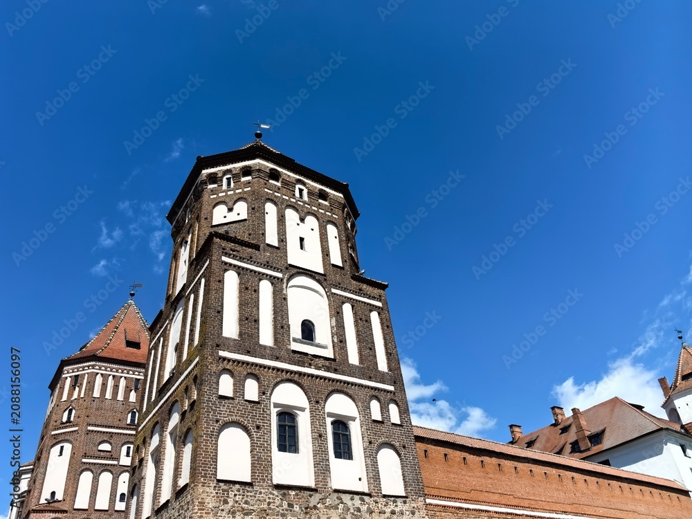 Fototapeta premium Horizontal low angle wide shot of the majestic Mir Castle complex brick towers and defensive walls under a blue sky, Belarus