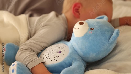 Little boy is sleeping with his toy a blue bear in bed. 4K