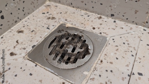 Fotografie Close-up of a dirty and clogged shower drain on a tiled floor, full of dust, dirt, and hair