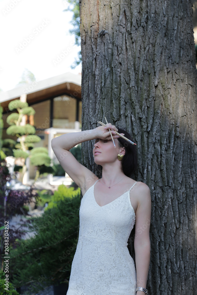 Obraz premium Woman in white dress holding paintbrush outdoor scene. Female creativity concept in outdoor garden portrait