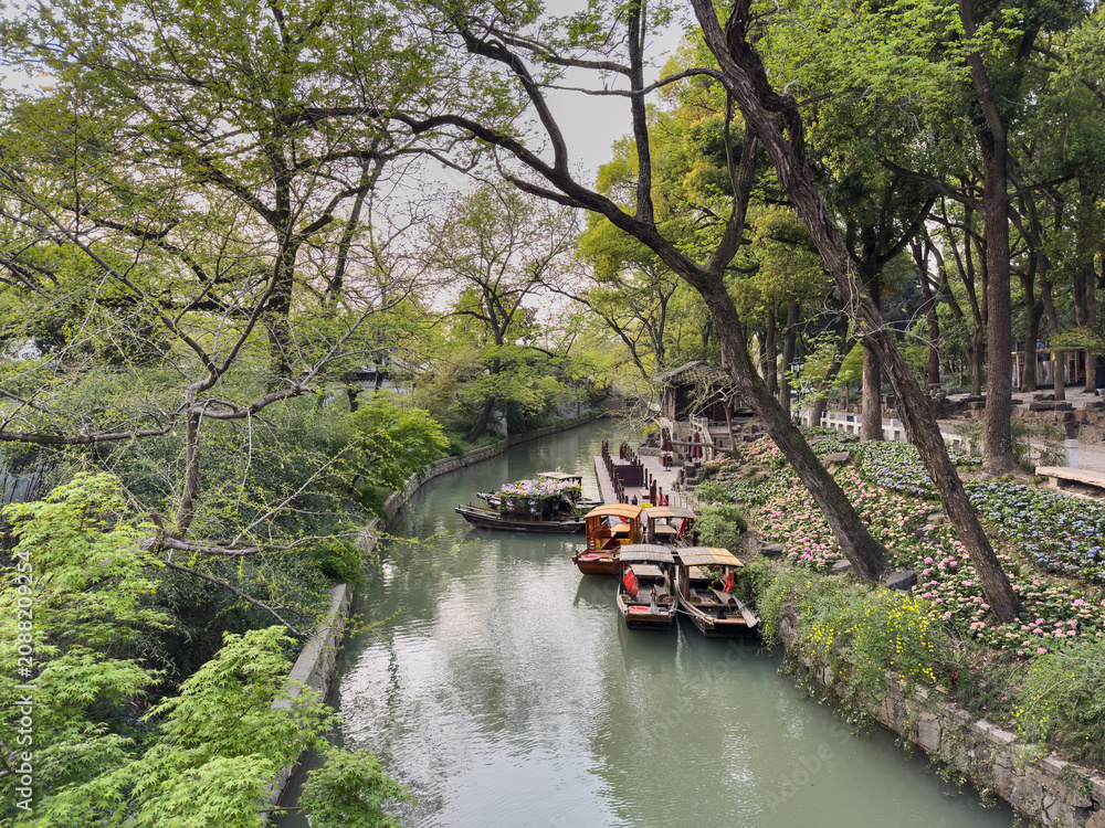 Naklejka premium Wooden boats moored on spring canal with flowers at Tiger Hill, Suzhou, Jiangsu, China