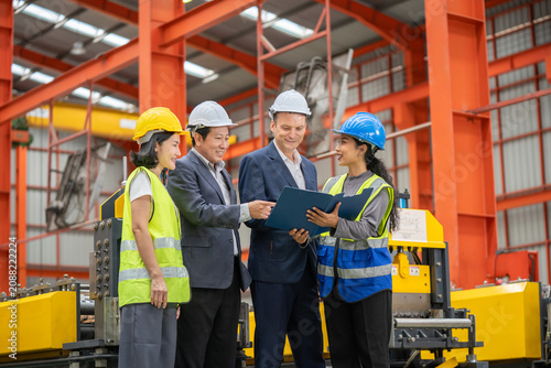 Diverse team of professionals working together in a contemporary industrial warehouse while wearing safety equipment