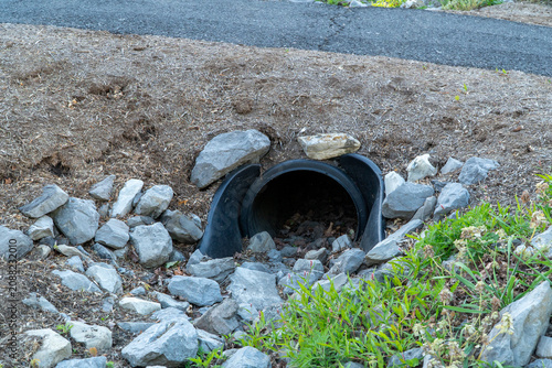 фотографія Black plastic culvert drain pipe installed in a rocky, mulched embankment beside an asphalt road, providing essential drainage in a natural outdoor setting