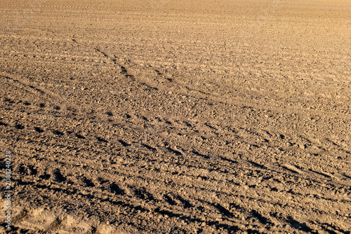 Tractor leaves clear tracks on freshly plowed dirt field in bright sunlight showing agricultural work done