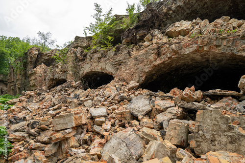 Rubble fills an area around old stone ruins with plants and trees growing nearby on a cloudy day in the countryside