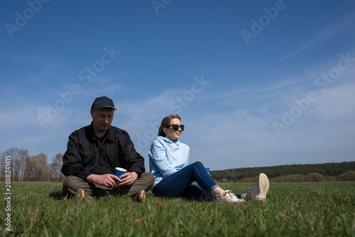 Couple sitting on green grass under a blue sky, enjoying coffee and a peaceful spring day outdoors, relaxing together in open countryside for a casual weekend picnic