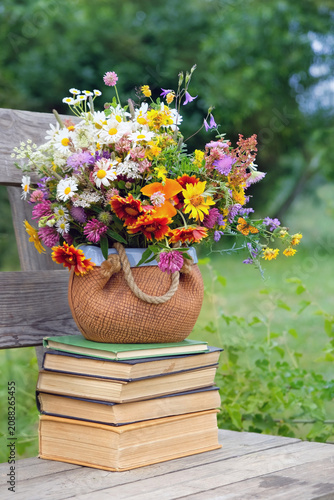 bouquet of bright colorful flowers on stack of books on wooden bench in garden. beautiful floral rustic composition in summer day. romantic, inspiration, relax peaceful atmosphere. Reading time