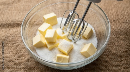 Butter cubes and sugar in a glass bowl with electric mixer beaters