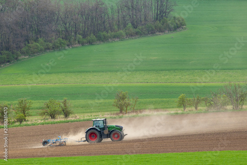 Green tractor cultivating dusty field in Jihomoravsky kraj