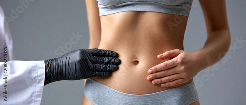 Lipoaspiração e contorno corporal. Doutor examinando a barriga de uma jovem paciente de roupa íntima cinza. Medicina estética e saúde