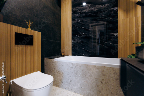 Modern bathroom with freestanding bathtub, black marble wall, vertical wooden paneling, neutral stone surfaces, and soft warm lighting creating serene upscale residential interior