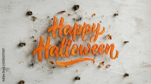 Handwritten Halloween greeting in orange on fresh snow with scattered autumn leaves