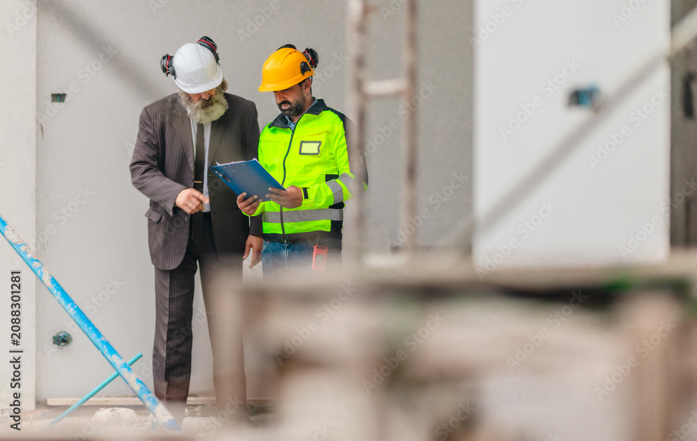 Fototapeta premium Engineer and businessman inspecting house construction site while discussing building project
