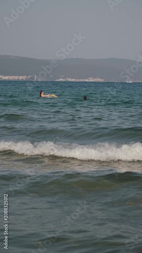 A teenager on an inflatable ring, immersed in a serene marine environment among gentle waves and distant hills