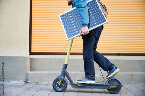 Bild auf Leinwand Cropped view of man rides electric scooter while carrying solar panel