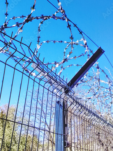 Razor Wire On Security Fence Against Clear Blue Sky Barrier And Protection Concept.