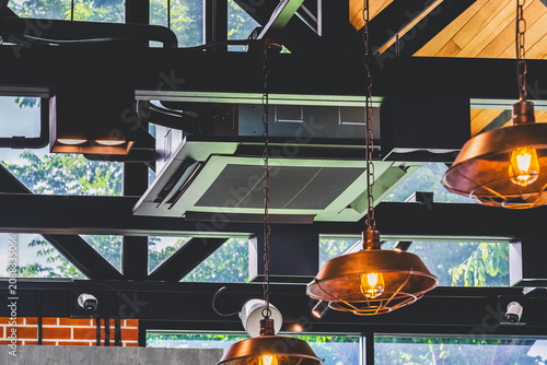 Modern cassette type air conditioner installed on loft ceiling with steel beams and wooden roof. Ceiling-mounted cassette air conditioning unit integrated into modern interior design. HVAC systems.