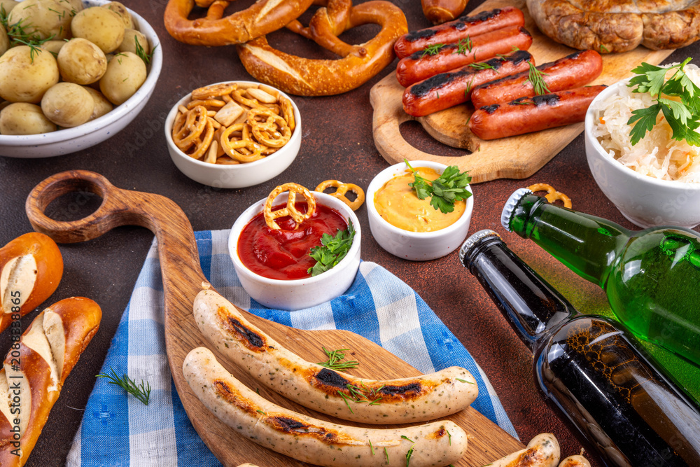 Fototapeta premium Oktoberfest picnic and barbecue food, bavarian party menu, bavarian sausages, pretzels, potato, sauerkraut, beer bottles, with picnic basket, checkered napkin tablecloth, Oktoberfest festive ribbon