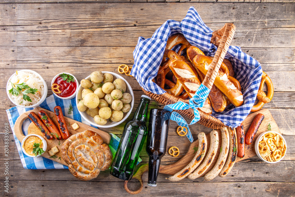 Fototapeta premium Oktoberfest picnic and barbecue food, bavarian party menu, bavarian sausages, pretzels, potato, sauerkraut, beer bottles, with picnic basket, checkered napkin tablecloth, Oktoberfest festive ribbon